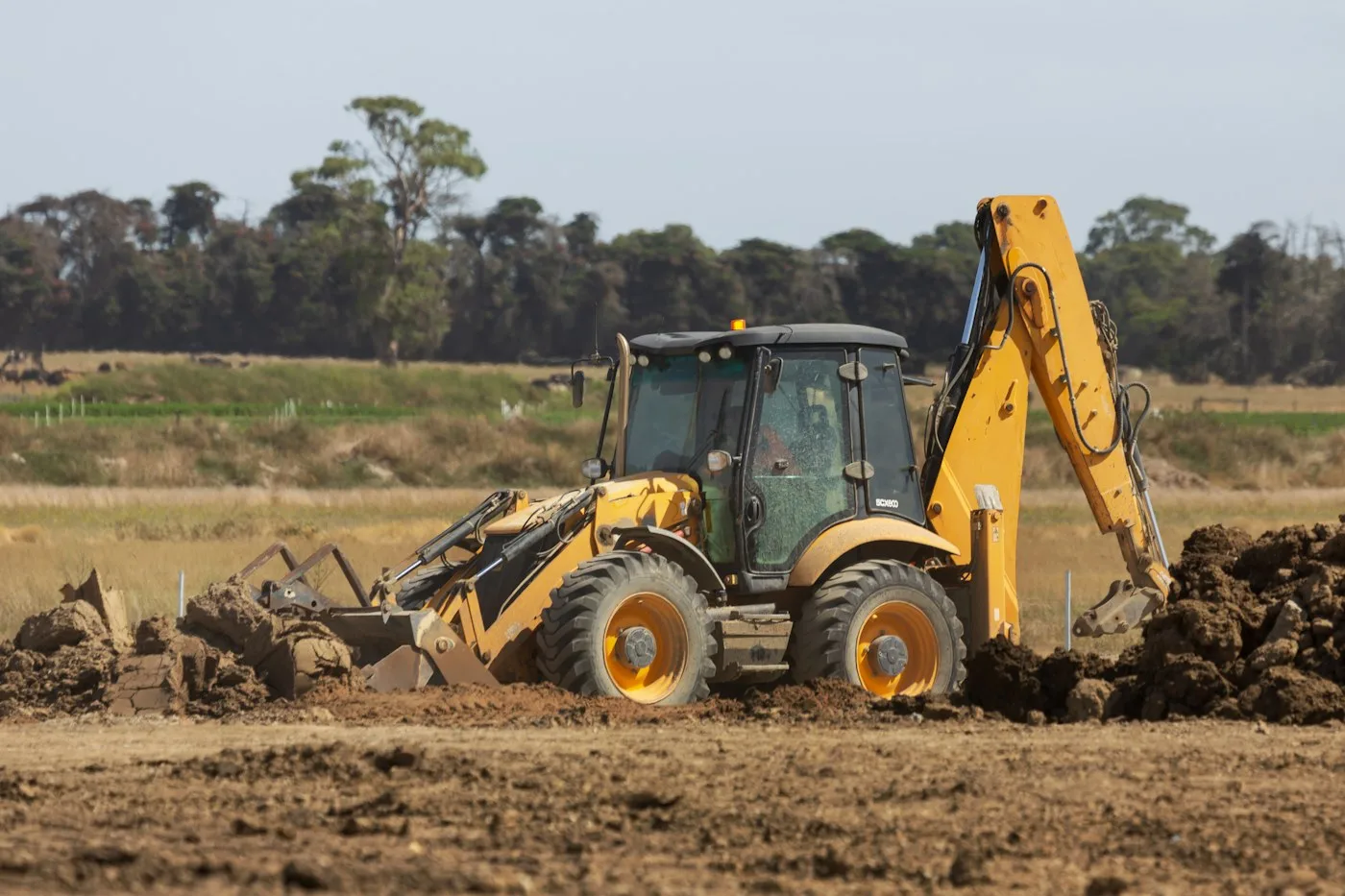 Backhoe loader on disturbed soil beside a field